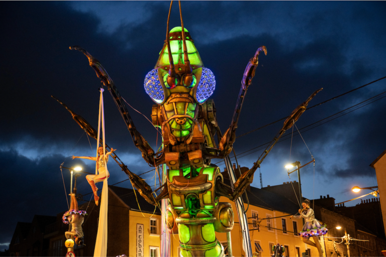 Aerial acrobats suspended from a giant outdoor insect scultpture