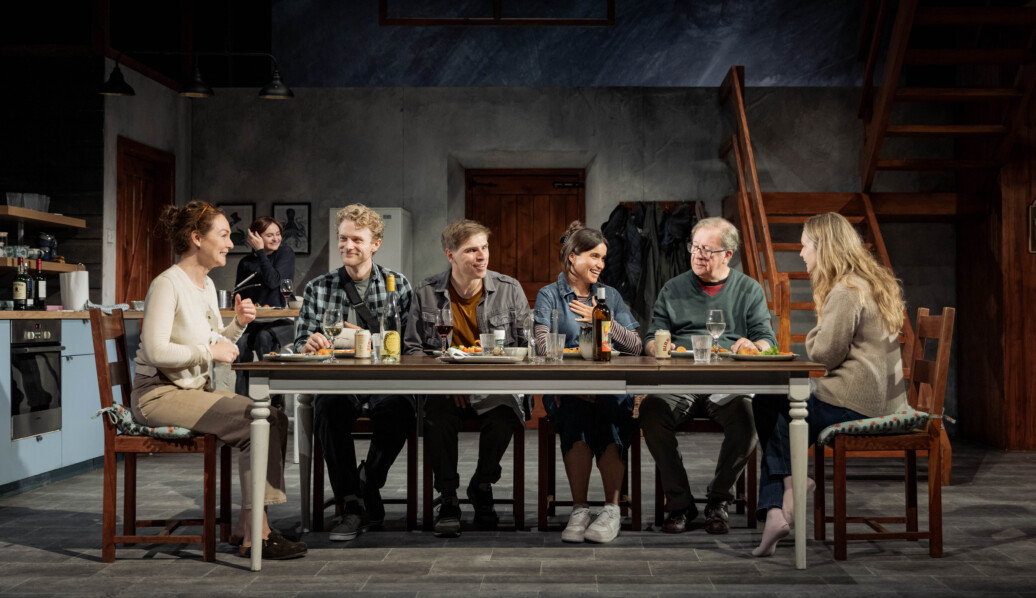 Reunion cast sits at table on the stage